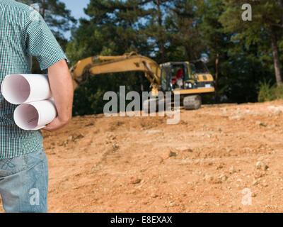 closeup of back view of standing engineer holding plans on outdoors constrution site Stock Photo