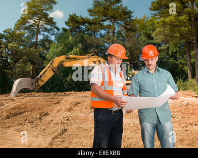 two caucasian engineers on construction site looking at plan and discussing it Stock Photo