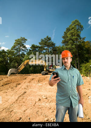 engineer looking at mobile phone holding blueprints on construction site Stock Photo