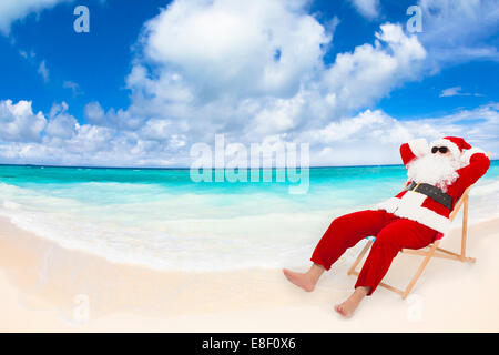 Santa Claus sitting on beach chairs with blue sky and cloud. Christmas holiday concept. Stock Photo