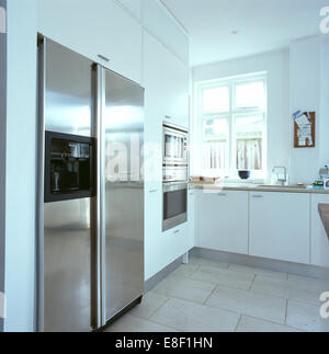 Large American-style stainless-steel refrigerator in modern white kitchen with limestone flooring Stock Photo