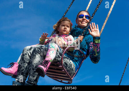 Mother with daughter enjoying life on the chain swing carousel, amusement park happy family Stock Photo