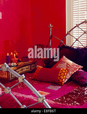 Bright pink silk hand made cover and Indian silk cushions on Gothic style metal bed in red economy style bedroom Stock Photo