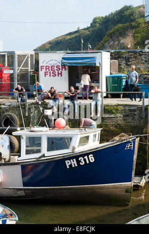 Fishing boat / boats moored / tied up in front of a kiosk / shop selling fresh fish at the sea harbour / Mevagissey harbor in Cornwall. UK. Stock Photo