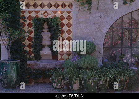 Tiled surround on alcove with stone urn in courtyard with green plants in glazed rustic pots Stock Photo