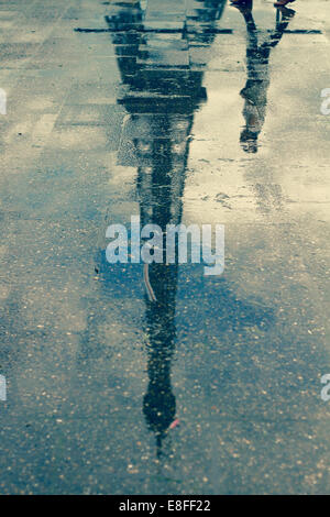 Reflection of man walking past Eiffel Tower in a puddle, Paris, France Stock Photo