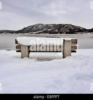 Snow covered bench by fjord, Norway Stock Photo