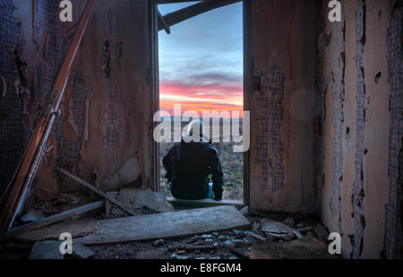 USA, Idaho, Rear view of man sitting on doorstep looking at sunset Stock Photo