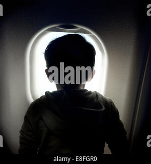 Boy looking through window on airplane Stock Photo