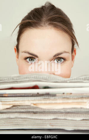 Young woman peeking over the top of a stack of newspapers Stock Photo