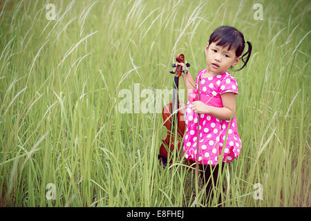 Girl standing in meadow holding violin Stock Photo