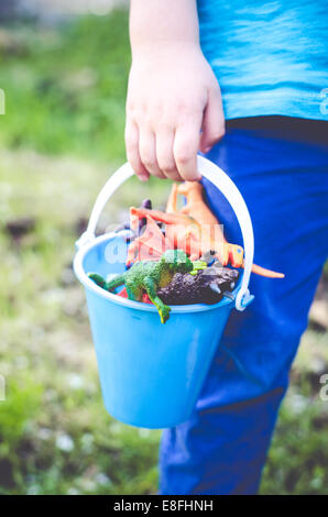 Boy holding bucket of plastic dinosaur toys Stock Photo