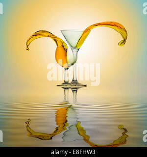 Yellow water splashing from two glasses standing side by side on water surface Stock Photo