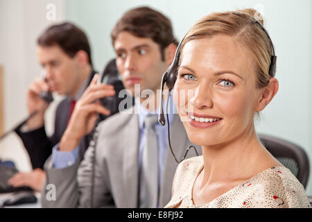 Portrait of a young woman with a telephone headset in an office with two coworkers talking on the phone Stock Photo