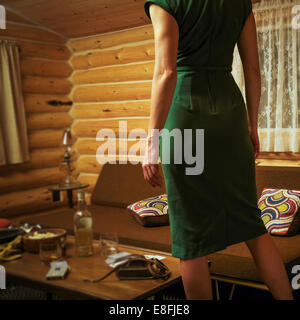 Canada, Alberta, Cochrane, Rear view of woman in mid-century styled log cabin wearing retro dress Stock Photo