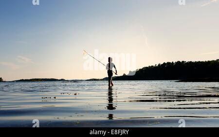 Silhouette of boy fishing at sunset, Tromoy, Arendal, Norway Stock Photo