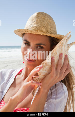 Young woman listening to conch shell on beach, Cape Town, Western Cape, South Africa Stock Photo
