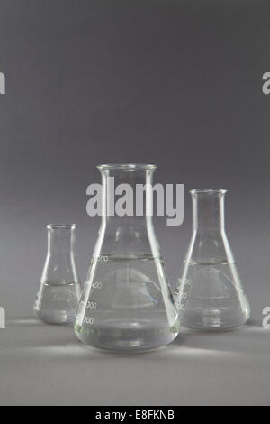 Three conical flasks and measuring beakers filled with clear liquid in a research laboratory Stock Photo