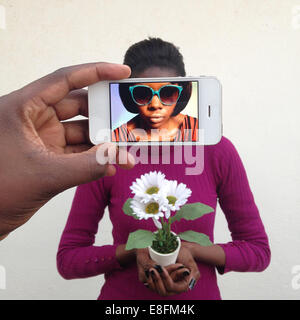 Man photographing a young woman using a mobile phone and seeing her alter ego on the screen Stock Photo