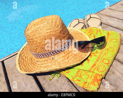 Straw hat, sunglasses, flip flops and sarong on wooden deck by swimming pool, Thailand