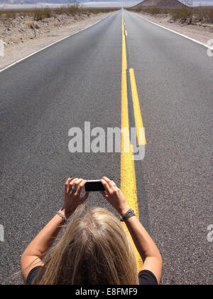 Woman taking photo of infinity road with mobile phone, Nevada, USA Stock Photo