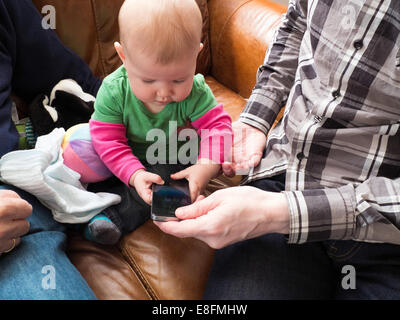 Baby boy sitting on sofa playing with his father's smart phone Stock Photo