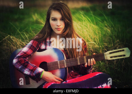 Portrait of a teenage girl sitting in a meadow with her guitar, Poland Stock Photo