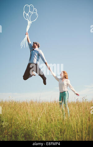 Woman standing in a meadow holding her boyfriends hand as he floats away holding balloons, Nashville, Tennessee, USA Stock Photo