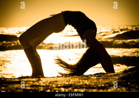 Silhouette of Woman practicing yoga backbend on beach Stock Photo