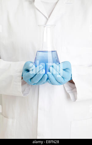 Close up of scientist holding a conical flask of blue liquid Stock Photo