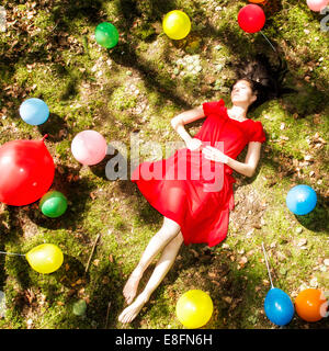 United Kingdom, England, Berkshire, Young woman with balloons sleeping in forest