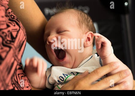 Baby boy yawning in his mother's arms Stock Photo