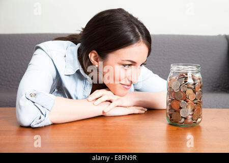 Young woman looking at jar full of coins Stock Photo