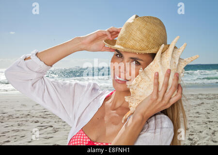Young woman listening to conch shell on the beach, Cape Town, Western Cape, South Africa Stock Photo