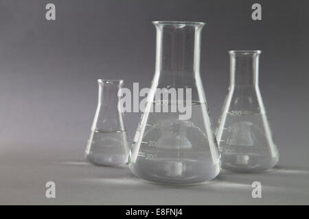 Three conical flasks and measuring beakers filled with clear liquid in a research laboratory Stock Photo