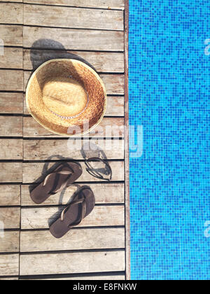 Sun hat, flip-flops and sunglasses by swimming pool