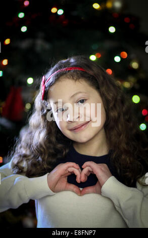 Girl making heart shape with hands in front of Christmas tree Stock Photo