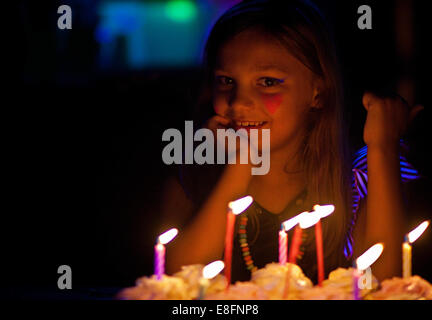 Smiling girl with heart shaped face paint sitting by her birthday cake Stock Photo