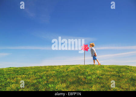 Boy standing in a meadow blowing a giant pinwheel Stock Photo