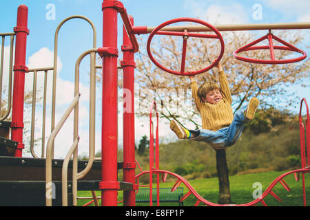 Happy boy hanging on a climbing frame in a garden Stock Photo
