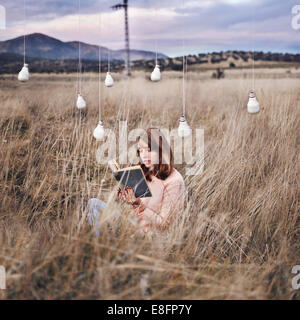 Woman sitting in a meadow under low energy light bulbs reading a book, Spain Stock Photo