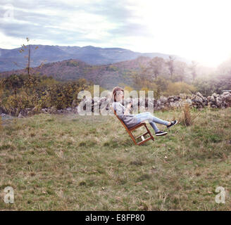 Woman sitting on a leaning chair in the garden with her digital tablet, Spain Stock Photo