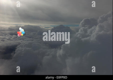 Bunch of multi coloured balloons flying in the sky above the clouds Stock Photo