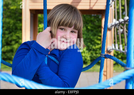 Young girl hanging in web of blue ropes Stock Photo