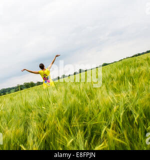 Rear view of woman in field with outstretched arms Stock Photo