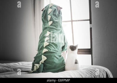 Rear view of a Shar pei dog wearing a dinosaur costume and British shorthair cat sitting next to each Stock Photo