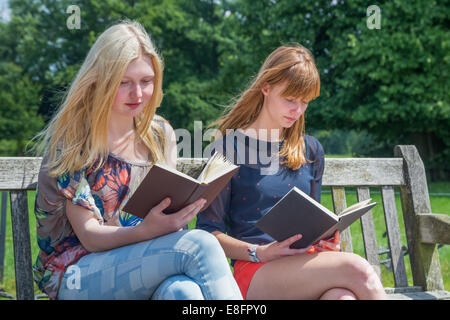 Two girls reading books on bench in park Stock Photo
