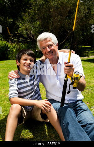 Grandfather and grandson sitting on a riverbank fishing Stock Photo