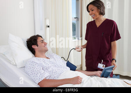 Nurse taking man's blood pressure in hospital Stock Photo