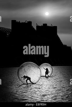 Silhouette of two children treading water in transparent spheres Stock Photo